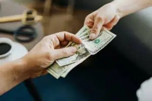 A close-up image of hands exchanging US dollar bills, symbolizing financial transaction or payment.