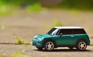 Green toy Mini Cooper car on pavement featuring a shallow depth of field outdoors.