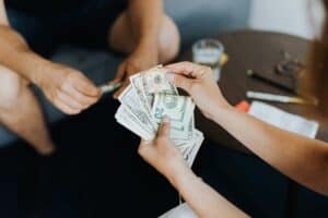 Close-up of people handling and counting US dollar bills indoors.
